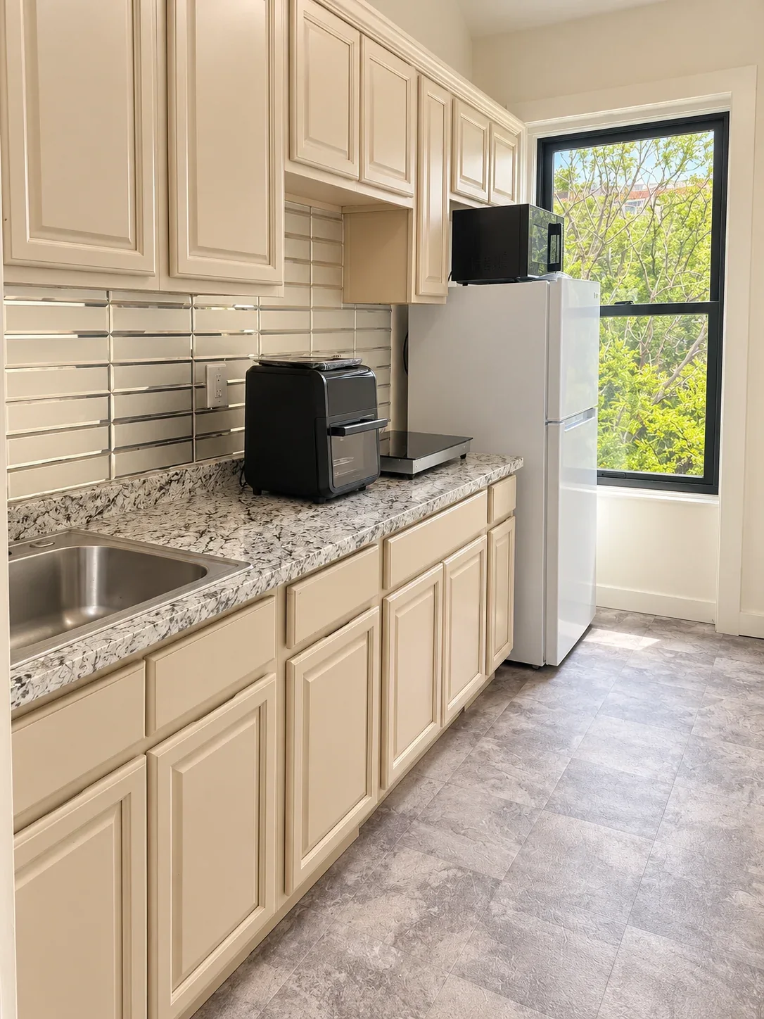 Bright kitchen with cream cabinets, marbled countertop and tile backsplash, clean floor and refrigerator